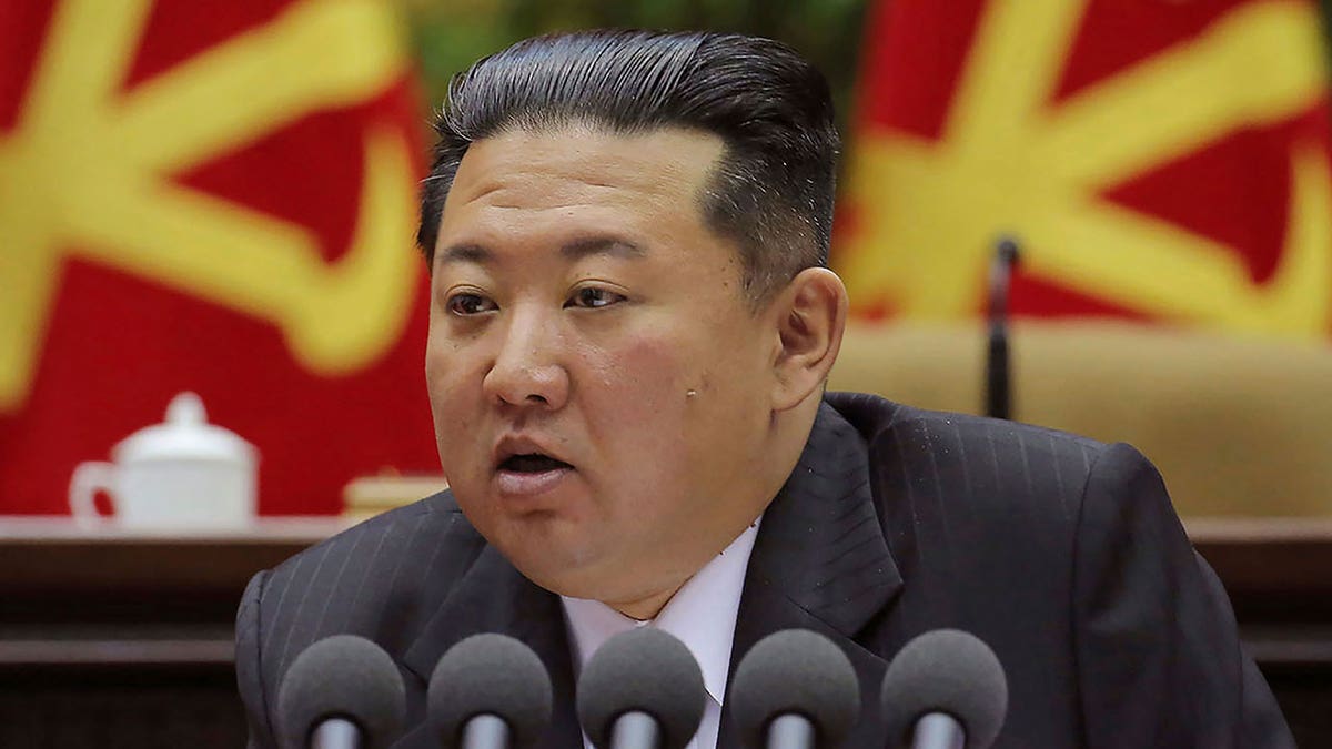 Kim Jong Un govori u nekoliko mikrofona dok sjedi ispred crvene i žute pozadine