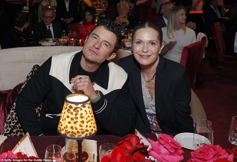 Orlando Bloom donned a black and white-colored jacket as he sat next to Katie Aselton at a table amid the festivities