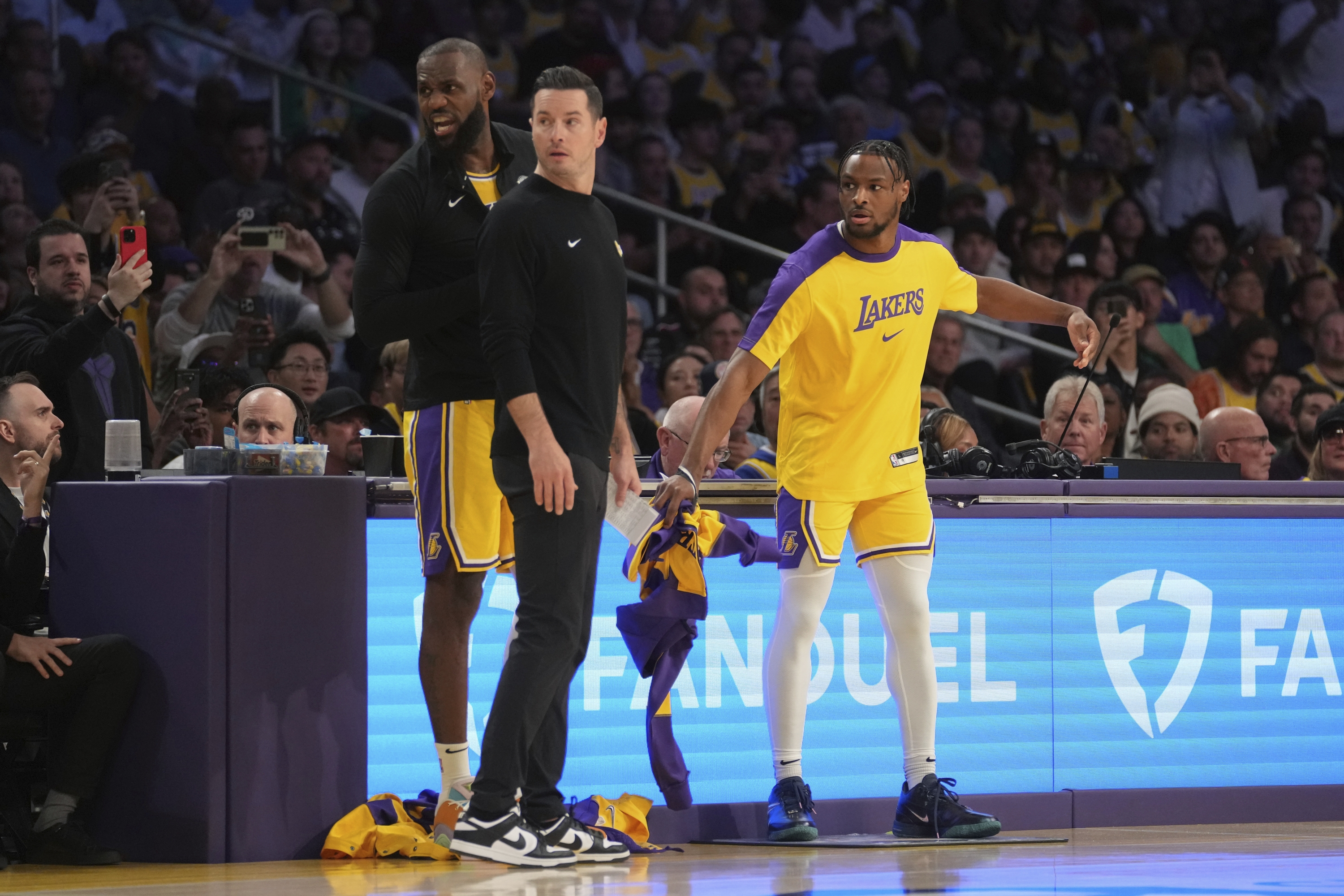 Napadač Los Angeles Lakersa LeBron James (23) i stražar Bronny James (9) prijavljuju se u igru ​​pored glavnog trenera JJ Redicka tijekom prvog poluvremena NBA košarkaške utakmice protiv Minnesota Timberwolvesa, utorak, 22. listopada 2024., u Los Angeles. (AP Photo/Eric Thayer)