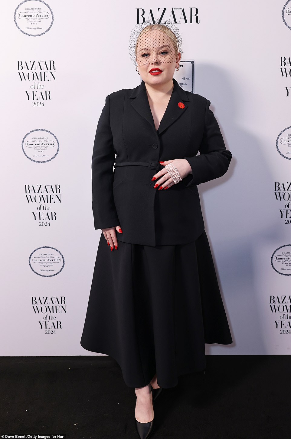 Nicola Coughla cut a chic figure in a sophisticated black blazer and a matching skirt, adding a vintage twist with a netted fascinator