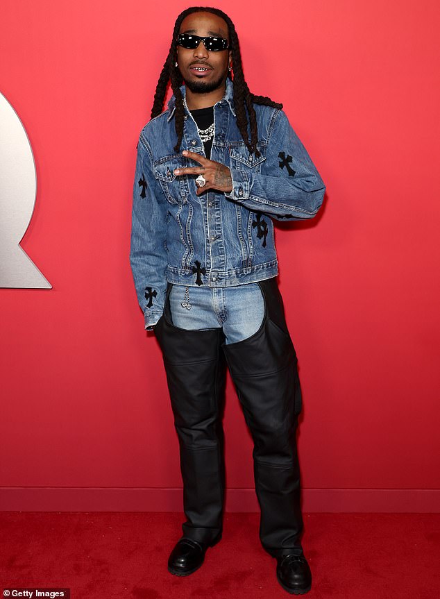 Quavo flashed a peace sign while wearing a denim jacket with black, cross-shaped embellishments as well as denim jeans