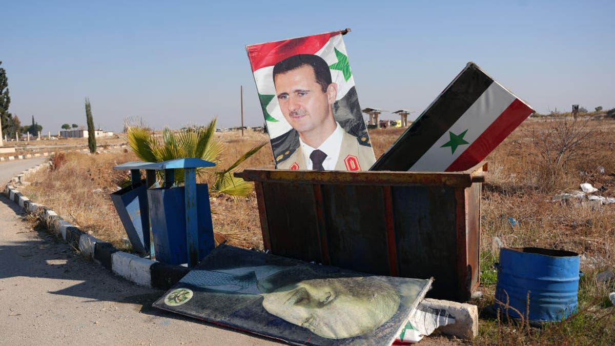TOPSHOT - Slika snimljena na ulazu u vojni aerodrom Kweyris u istočnom dijelu pokrajine Aleppo 3. prosinca 2024. prikazuje portret sirijskog predsjednika Bashara al-Assada i nacionalnu zastavu u kontejneru za smeće nakon preuzimanja oblasti od strane pobunjeničkih skupina.