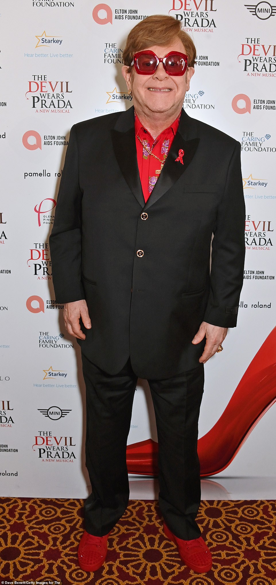Sir Elton continued to showcase his dramatic weight loss after embracing a healthier lifestyle in a tailored black Versace suit which he teamed with a red floral shirt, sparkly trainers and statement glasses