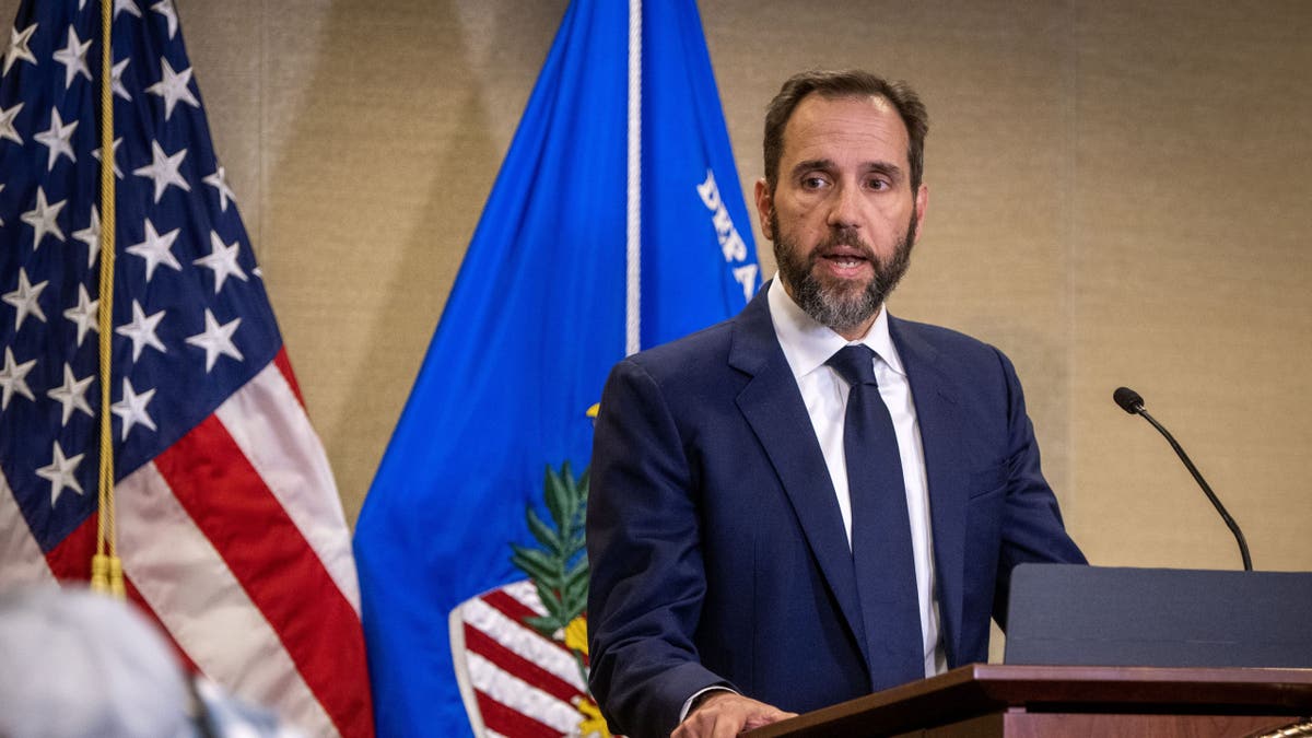 Jack Smith za govornicom sa SAD-om, zastave DOJ-a iza njega