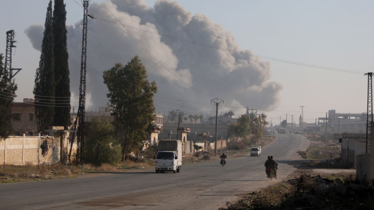 Borci ulaze u okrug Rashidin na periferiji Alepa na svojim motociklima s dimom koji kulja u pozadini tijekom borbi 29. studenog 2024., dok džihadisti Hayat Tahrir al-Sham (HTS) i savezničke frakcije nastavljaju svoju ofenzivu u pokrajini Aleppo protiv vladinih snaga . 