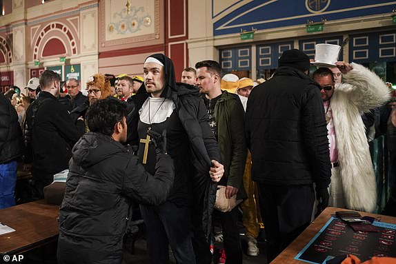 Fans dressed in costumes are seen around the fan village before the start of the quarter final match between Peter Wright of Scotland and Stephen Bunting of England, at the World Darts Championship in London, Wednesday, Jan. 1, 2025.(AP Photo/Alberto Pezzali)