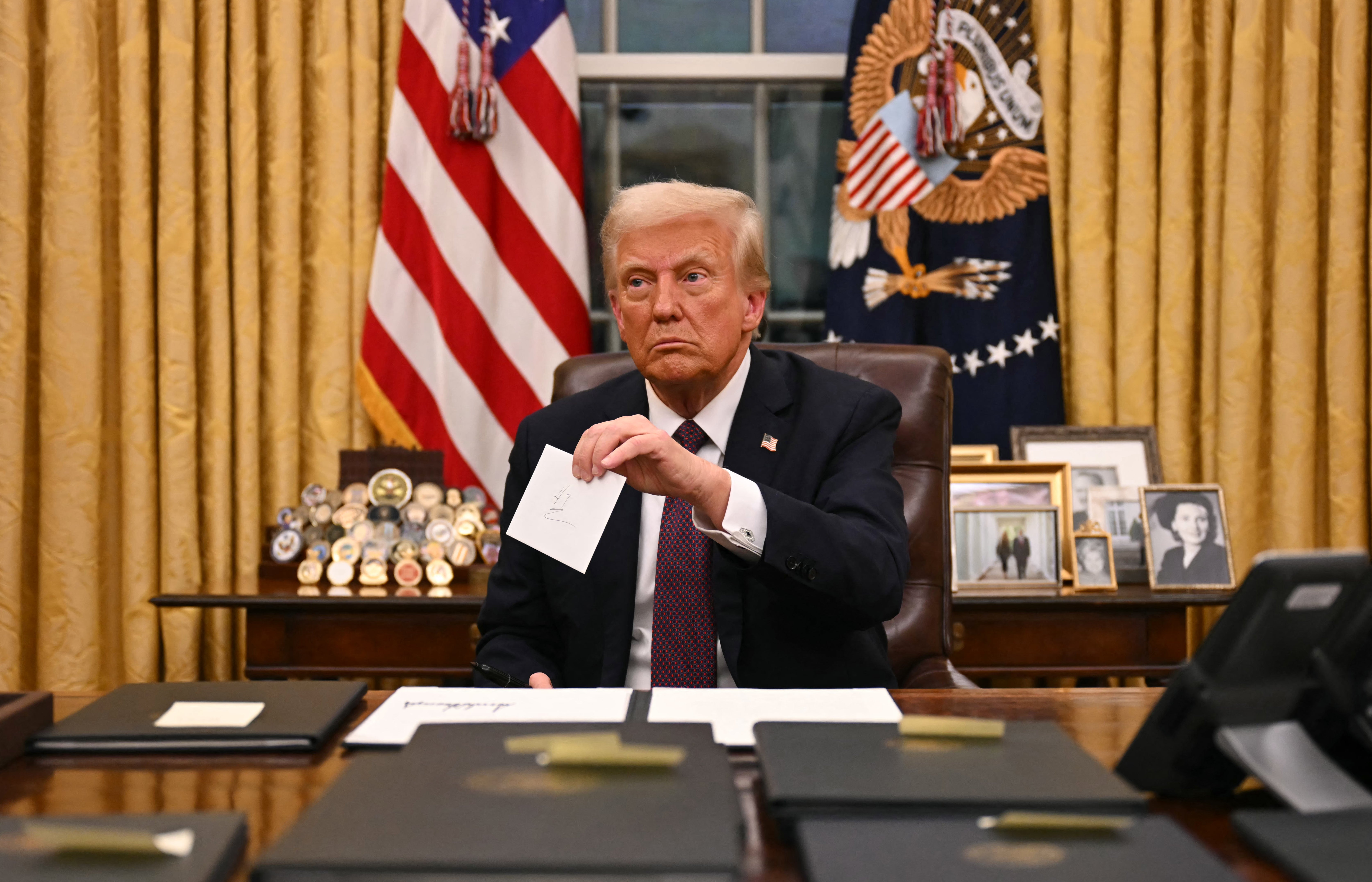 Američki predsjednik Donald Trump drži pismo odlazećeg predsjednika Joea Bidena dok potpisuje izvršne naloge u Ovalnom uredu