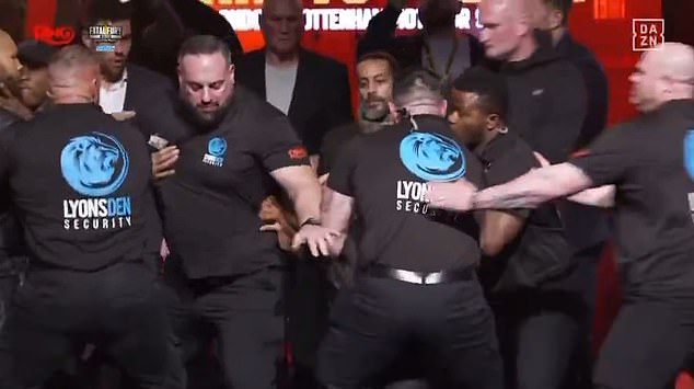 Tijekom svađe koja slijedi, Nigel Benn (krajnje lijevo, crna kapa) hvata Eubank Jnr za grlo