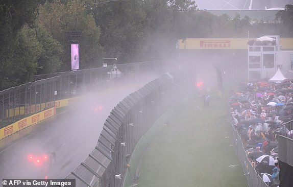 Gledatelji (R) sjede pod kišobranima kako bi se s kišom pokrivali kao povorka automobila Formule 2 prije Grand Prix -a Australian Formule 1 u krugu Albert Park u Melbourneu 16. ožujka 2025. (Foto William West / AFP) / - Slika ograničena na uredničku uporabu - strogo bez komercijalne upotrebe / AFP -a)