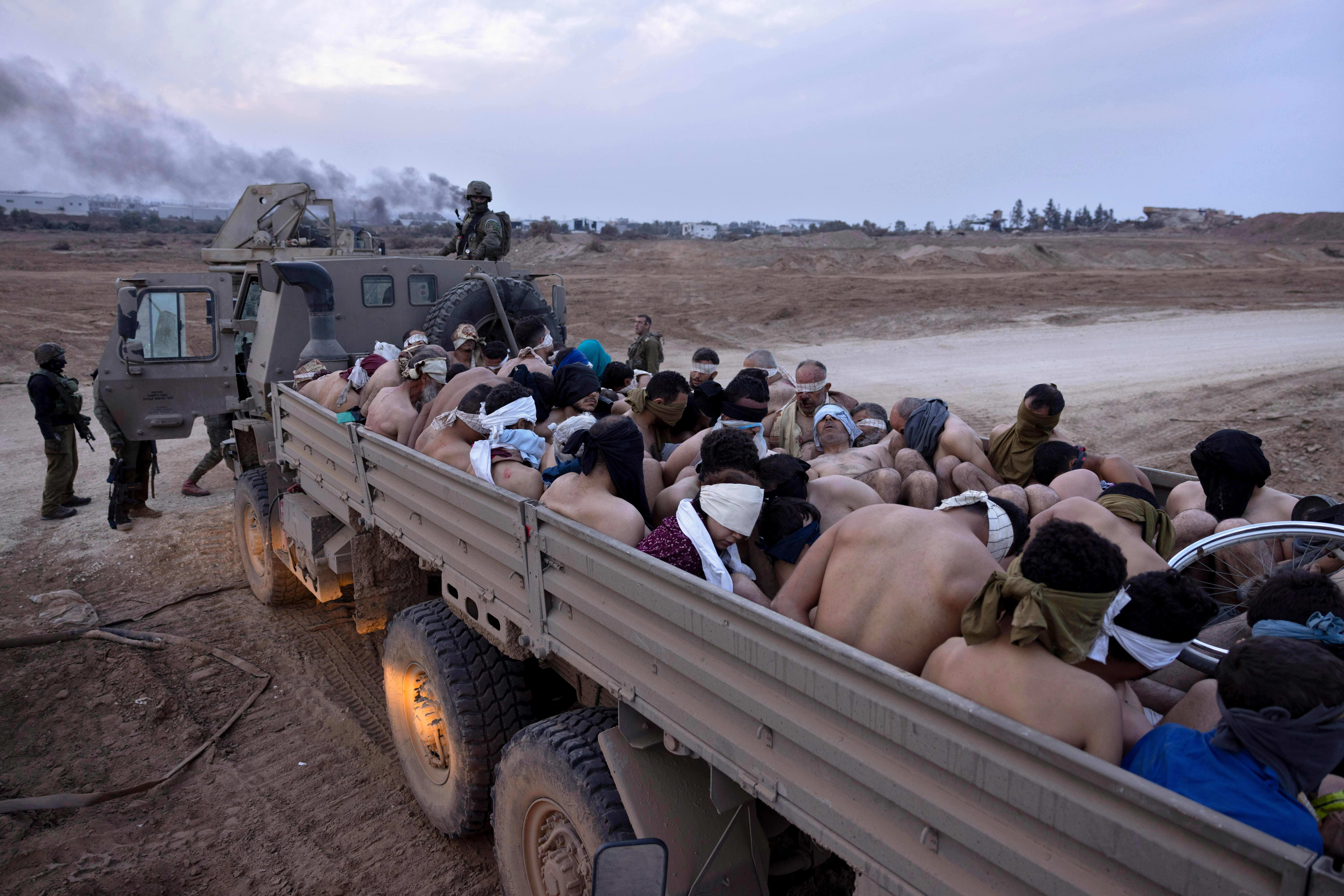 Israeli soldiers stand by a truck packed with bound and blindfolded Palestinian detainees, in Gaza, December 2023
