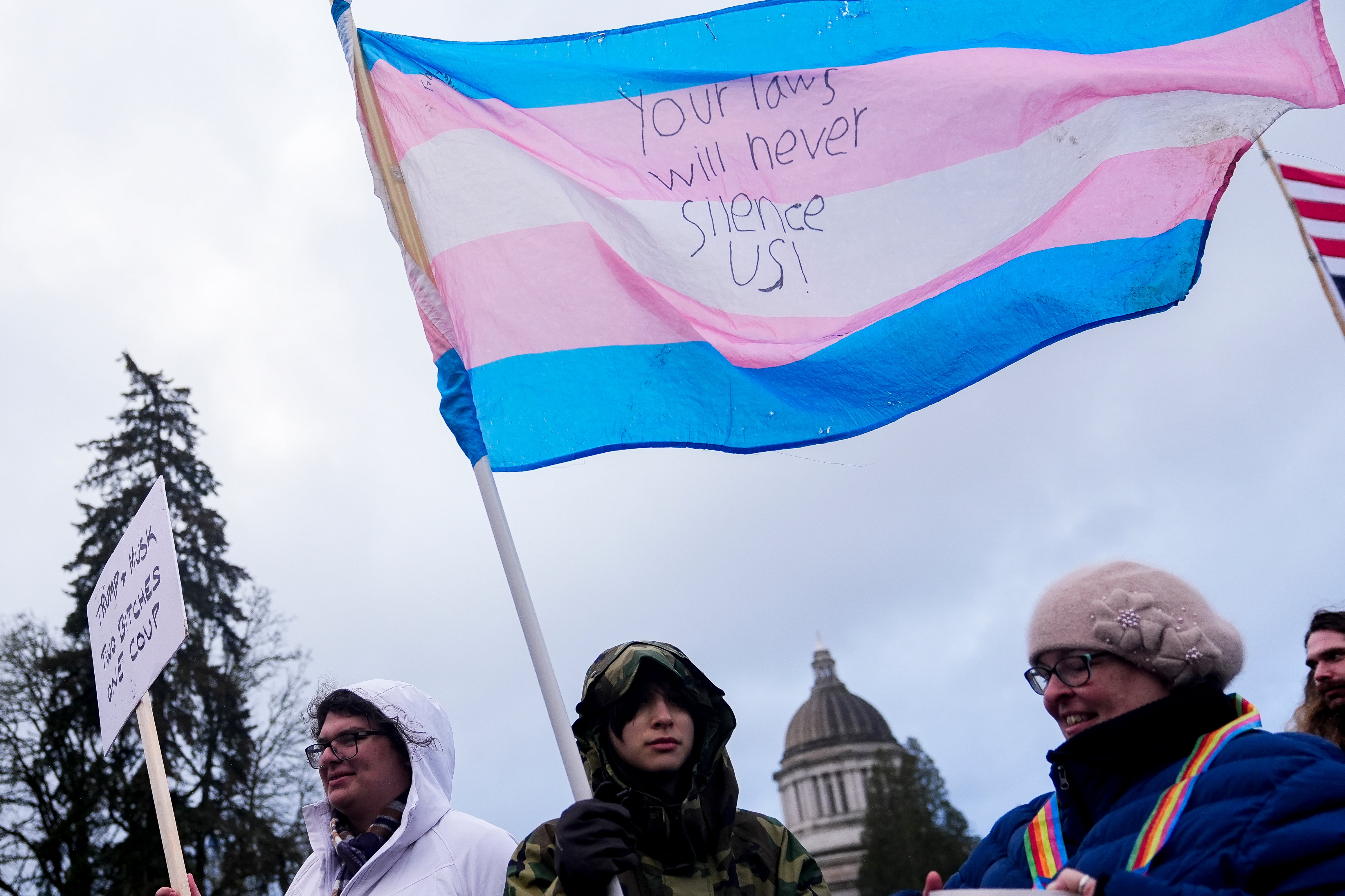 Fliv Y., Centar, drži zastavu transrodnih ponosa dok se ljudi okupljaju kako bi prosvjedovali protiv Trumpove administracije i projekta 2025. u blizini zgrade države Washington State Capitol, 5. veljače 2025. u Olympiji, Wash. (AP Photo/Lindsey Wasson, File)
