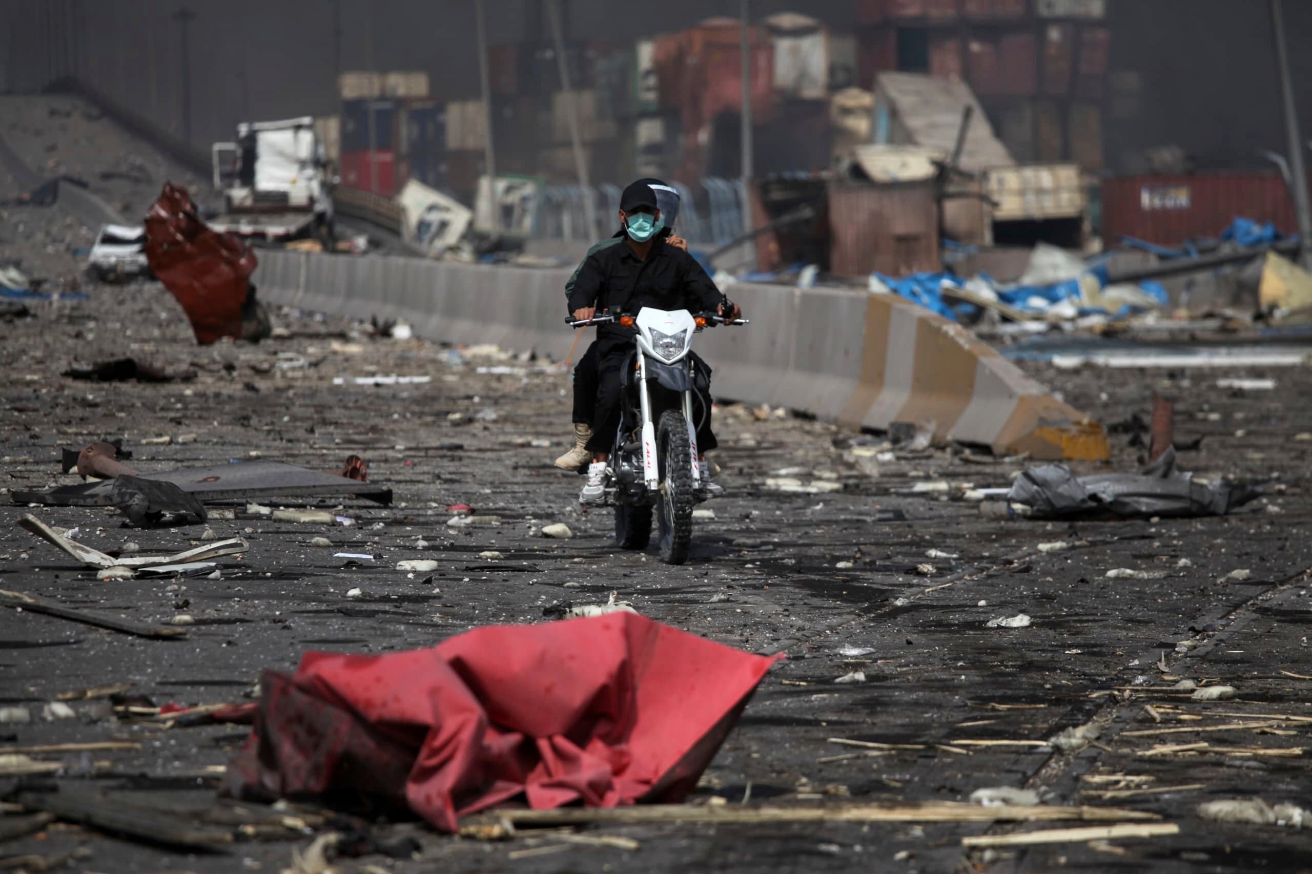 Dvojica muškaraca na motociklu voze se krhotinama nakon što je masivna eksplozija ljuljala luku u blizini južnog grada Bandar Abbas