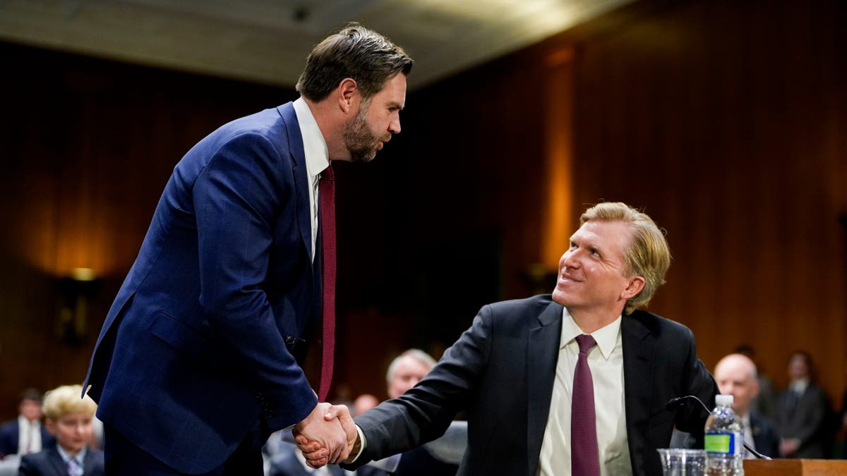 Potpredsjednik JD Vance rukuje se s Elbridgeom Colbyjem prije saslušanja odbora za oružane službe Senata, dok Colby sjedi za stolom svjedoka koji se smiješi Vanceu.
