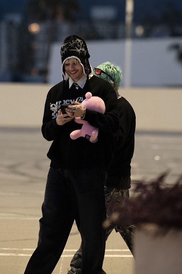 Aussie Rocker, 29, viđen je u prevelikoj crnoj kapuljači na slojevitoj preko prugaste košulje i ukrašen srebrnim nakitom, stežući ružičastu plišanu igračku dok se pomiče na telefonu