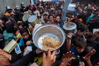 Palestinci se okupljaju kako bi primili topli obrok na točki distribucije hrane u kampu Nuseirat za izbjeglice u središnjoj traci Gaze
