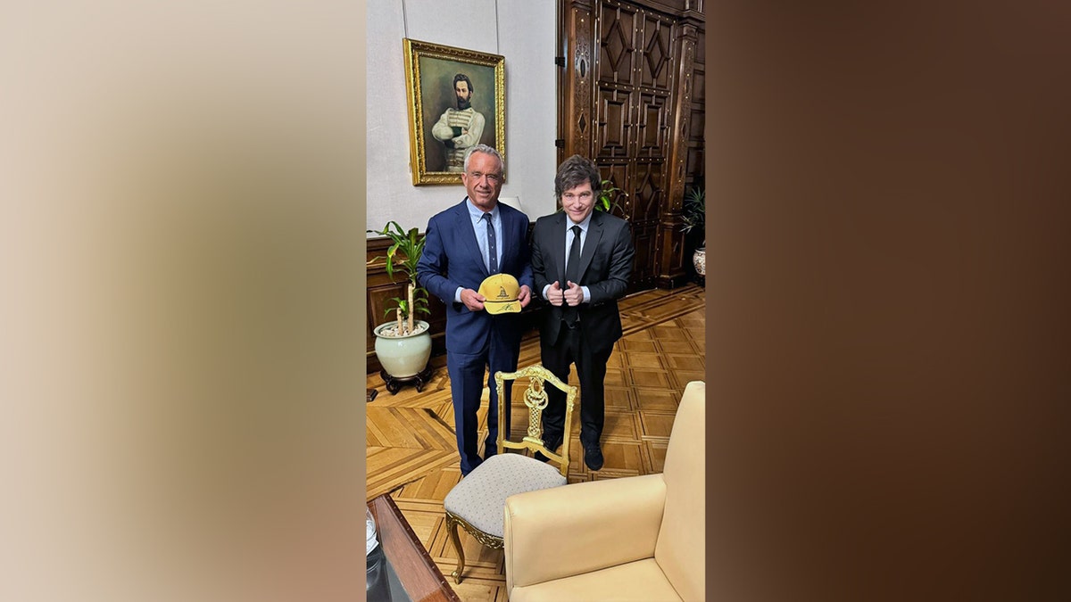 Kennedy i Milei poziraju sa žutom kapom s temom Gadsdena u formalnoj sobi s portretom u pozadini.