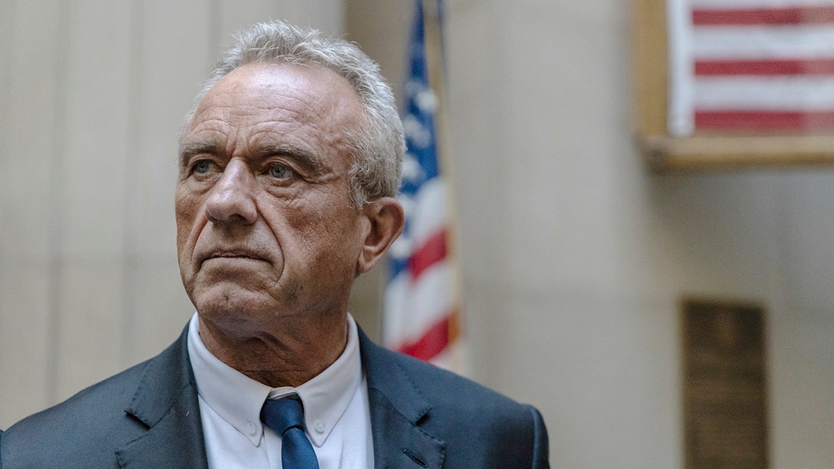 RFK JR koji stoji ispred američke zastave