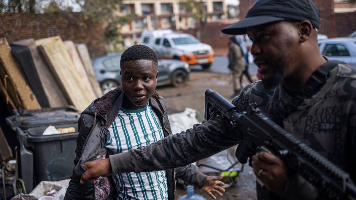 Policijski službenik u civilnoj odjeći u policijskoj upravi metroa u Johannesburgu dovodi u pitanje muškarca koji je pronađen u razrijeđenoj zgradi koja se 15. svibnja 2023. godine koristi kao sklonište u Johannesburgu.