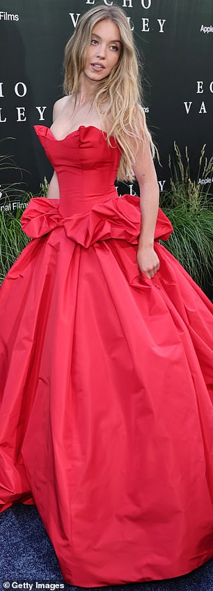 Njezina luksuzna grimizna froka bila je prikrivena oko njezine zavidno sjajne srednje presjeka prije nego što je prešla u luksuznu suknju koja je tekla po podu