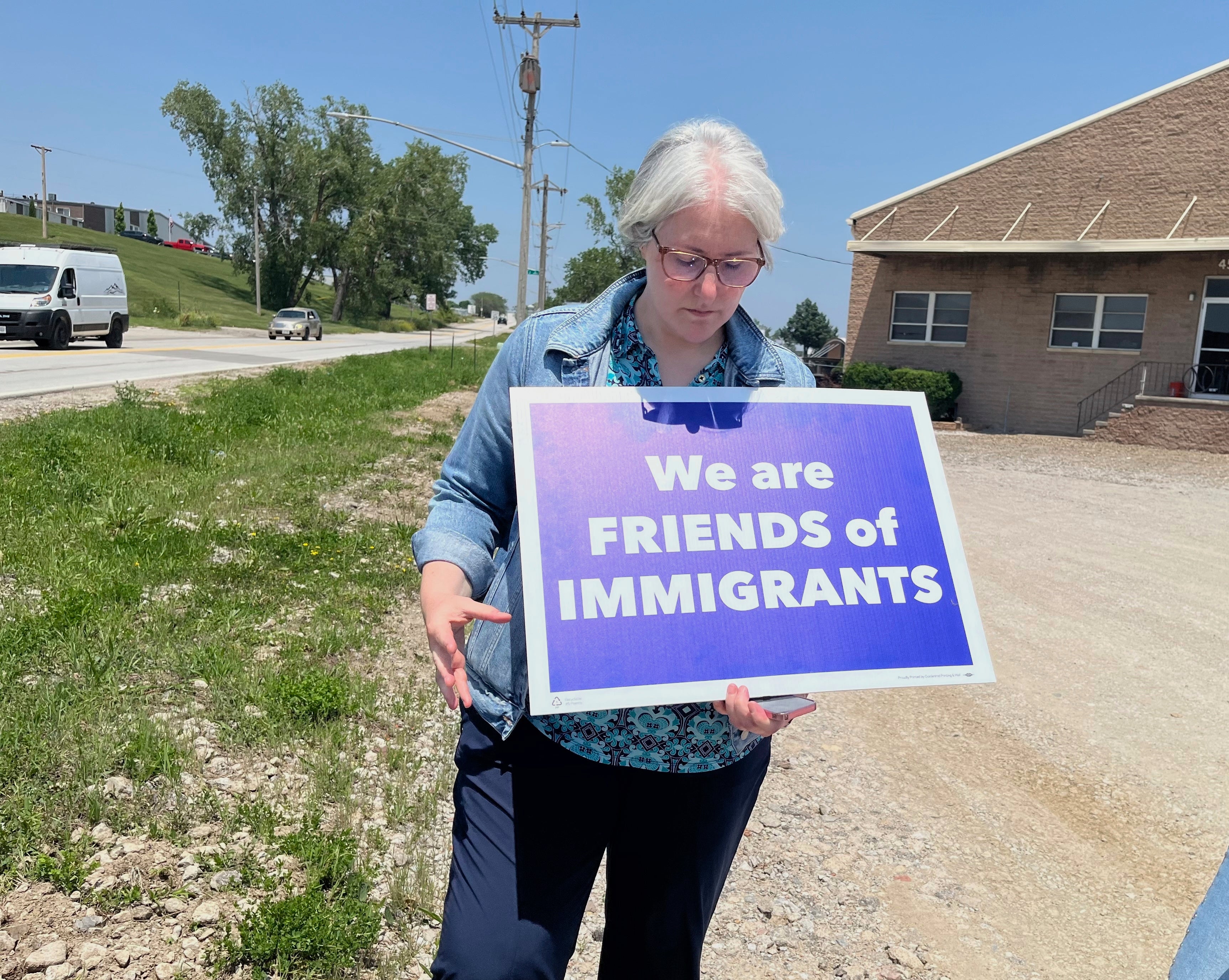 Sara Schulte-Bukowinski, vođa vjere u Omahi, Neb., Ima znak koji je prosvjedovao u imigracijskom raciji, utorak, 10. lipnja 2025., u Glenn Valley Foods, tvornici za pakiranje mesa u Južnoj Omahi. (AP Photo/Margery A. Beck)