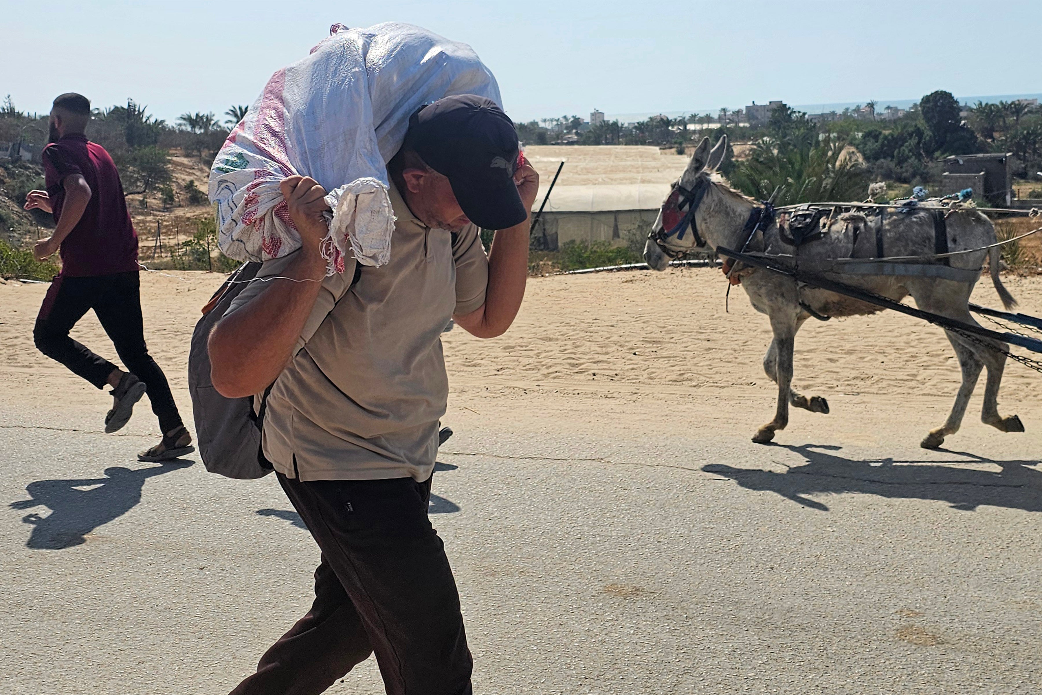 Čovjek hoda s vrećom na stražnjem dijelu vrata dok raseljeni Palestinci primaju humanitarnu pomoć u Rafahu