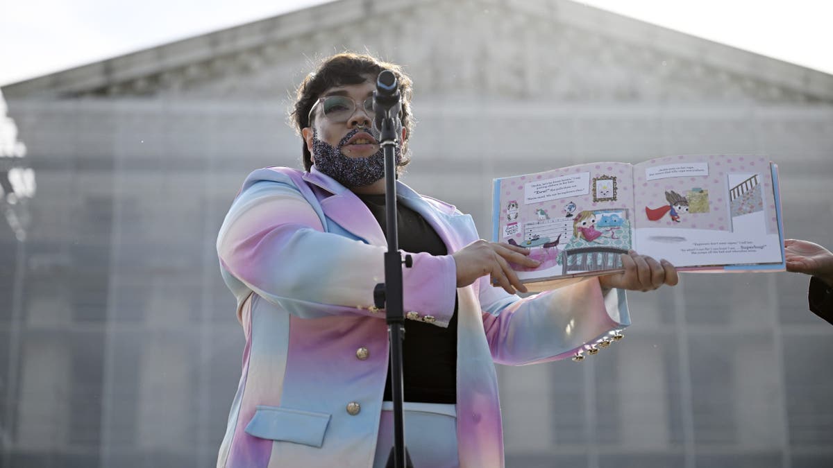 Govornik u povlačenju noseći pastelno dugačko odijelo čita dječju knjigu naglas na mikrofonu tijekom javnog događaja izvan Vrhovnog suda u SAD -u