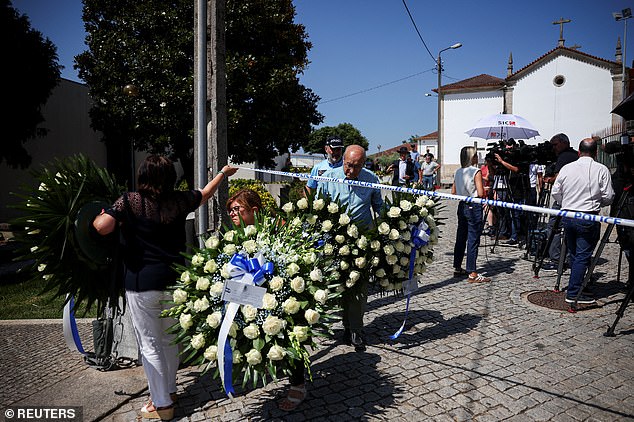 People carry wreaths of flowers under police tape under the chapel