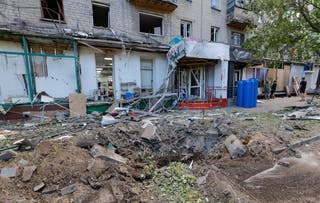 Ljudi pokrivaju slomljene prozore u oštećenoj stambenoj zgradi nakon granatiranja