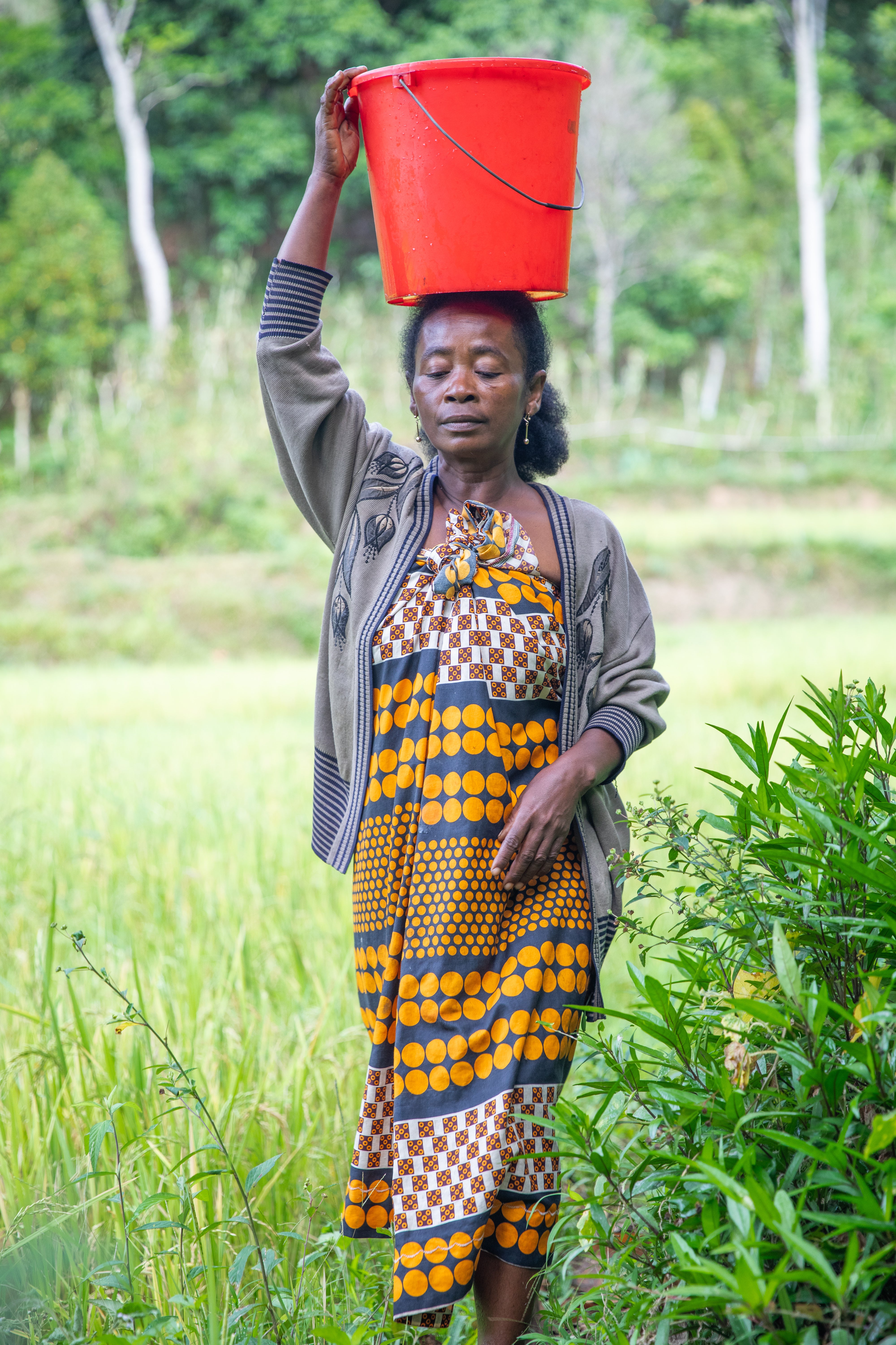 Edlyne, who does not yet have access to a water source in her village, is pictured walking home with a full bucket on her head