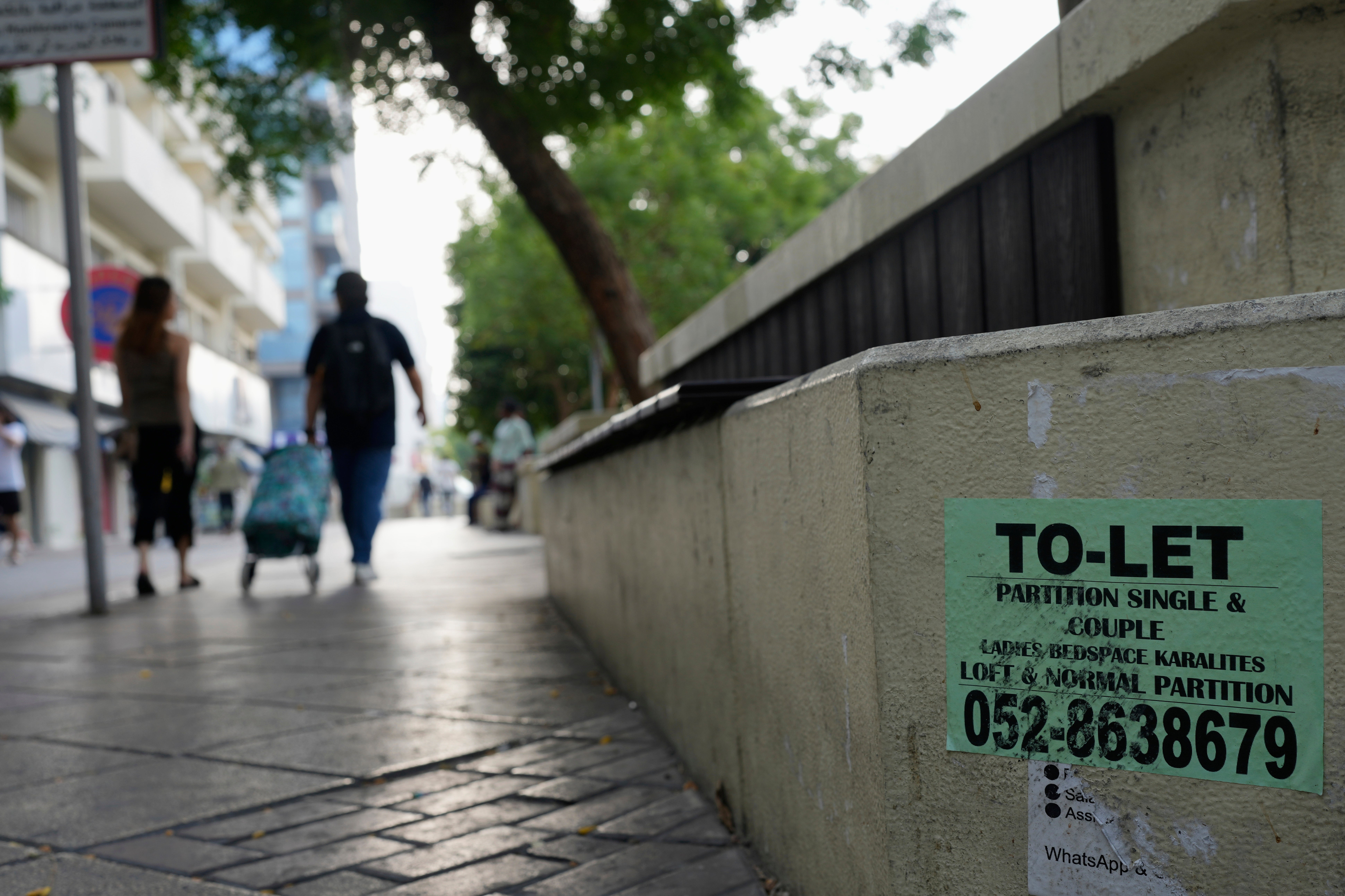 Ljudi prolaze pored betonske klupe omučene oglasima za jeftino, podijeljeno stanovanje u Dubaiju, Ujedinjeni Arapski Emirate, petak, 4. srpnja 2025. (AP Photo/Altaf Qadri)