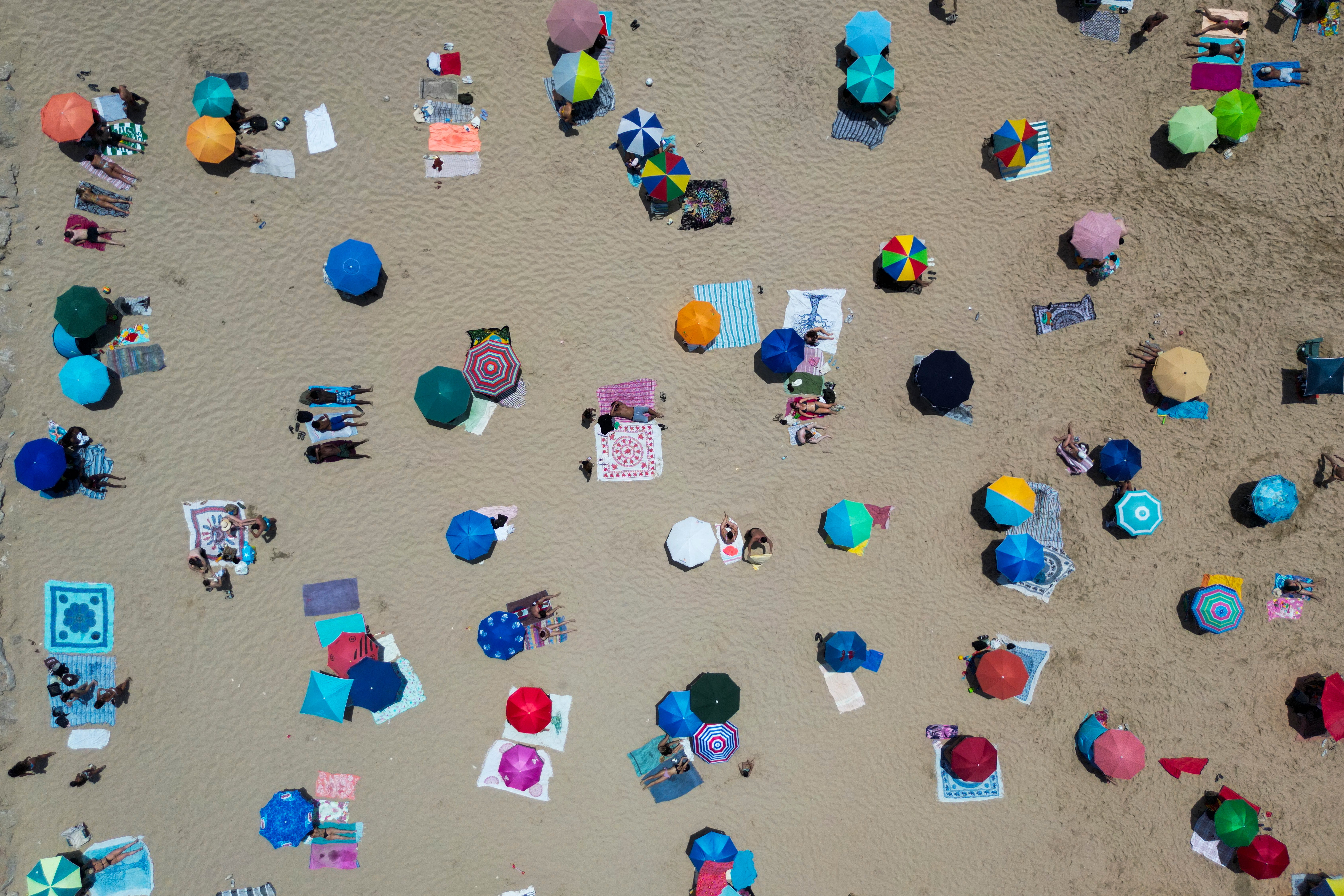 Ljudi sjede pod Umberllasom na plaži Costa da Caparica u Almadi, u blizini Lisabona, u nedjelju