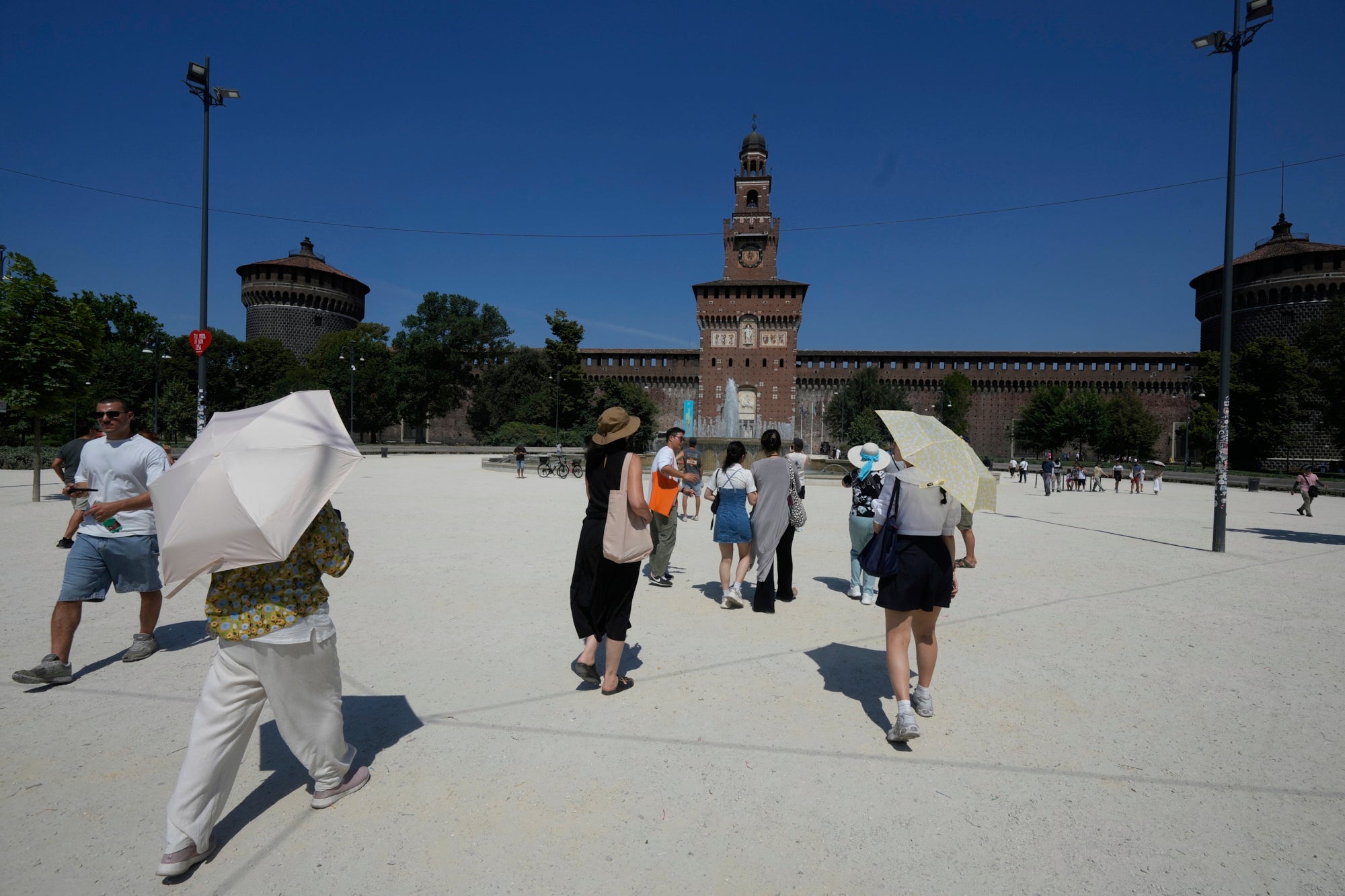 Turisti pokrivaju s vrućeg sunca kišobranima ispred dvorca Sforzesco, u Milanu