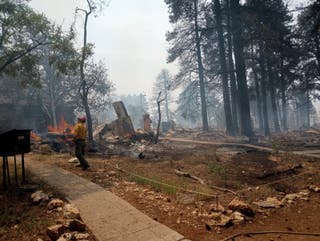 Vatrogasac stoji u blizini krhotina i aktivnog plamena uslijed ugljenisanih ostataka spaljene strukture u blizini lože Grand Canyon u Arizoni, u SAD -u, 13. srpnja 2025. godine.