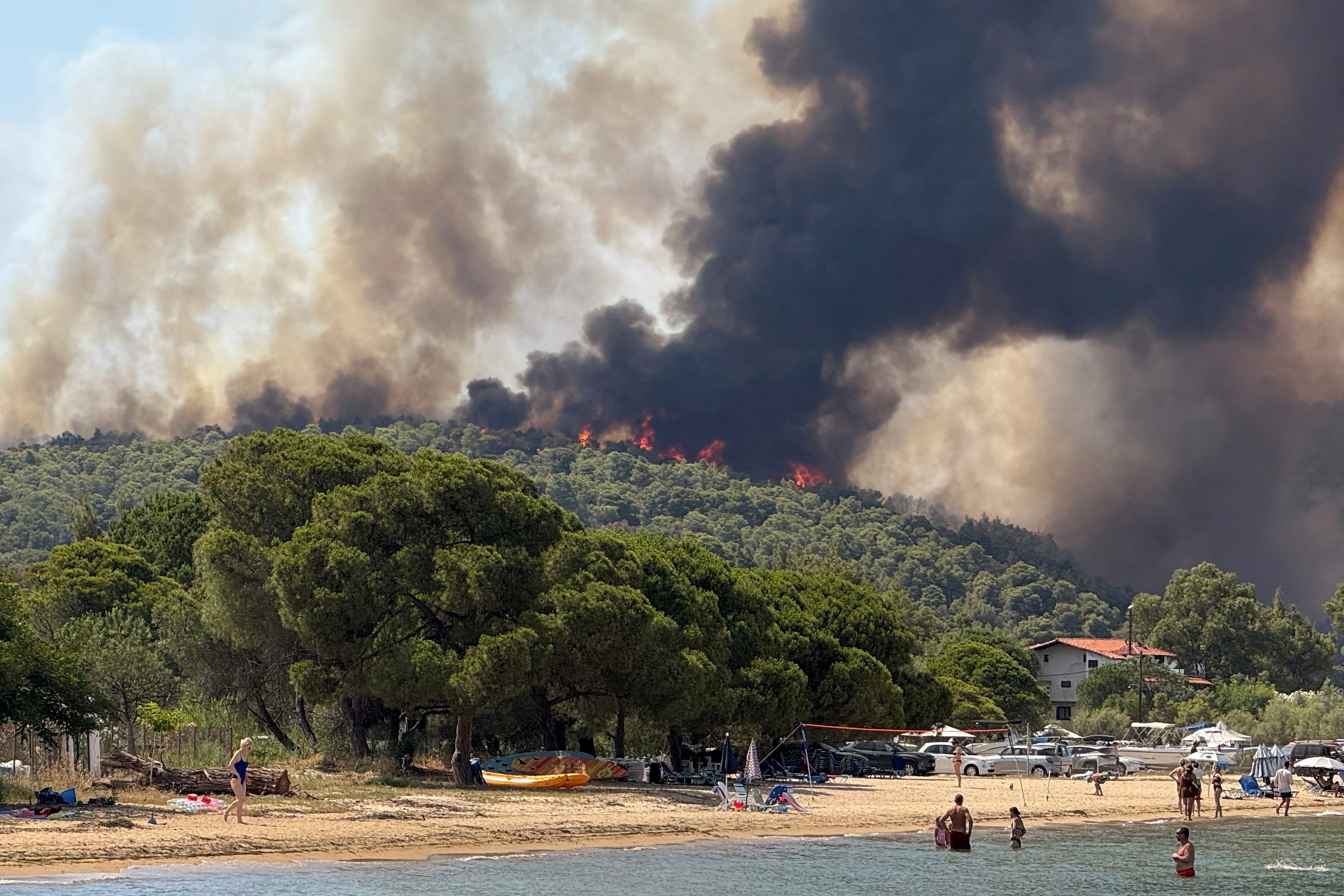 Plažari gledaju na rastući plamen i dim od požara koji gori u selu Vourvourou na poluotoku Halkidiki, Grčka, 2. srpnja 2025.