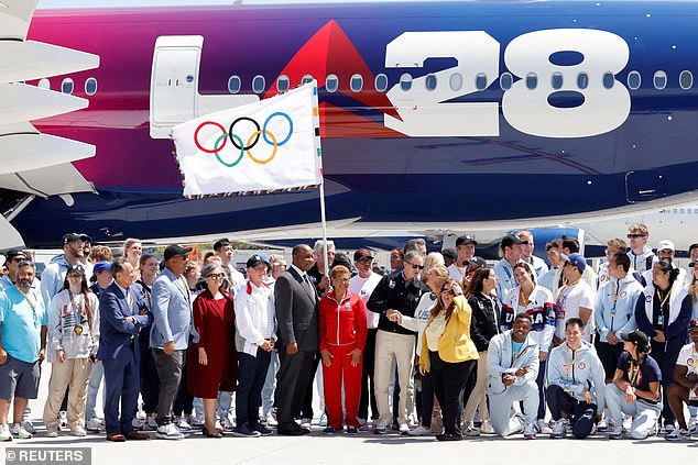 Ova fotografija 2024. prikazuje članove LA28, službenici lokalne samouprave i američki olimpijski sportaši poziraju se sa službenom olimpijskom zastavom dok se prvi put vraća u Los Angeles u 40 godina