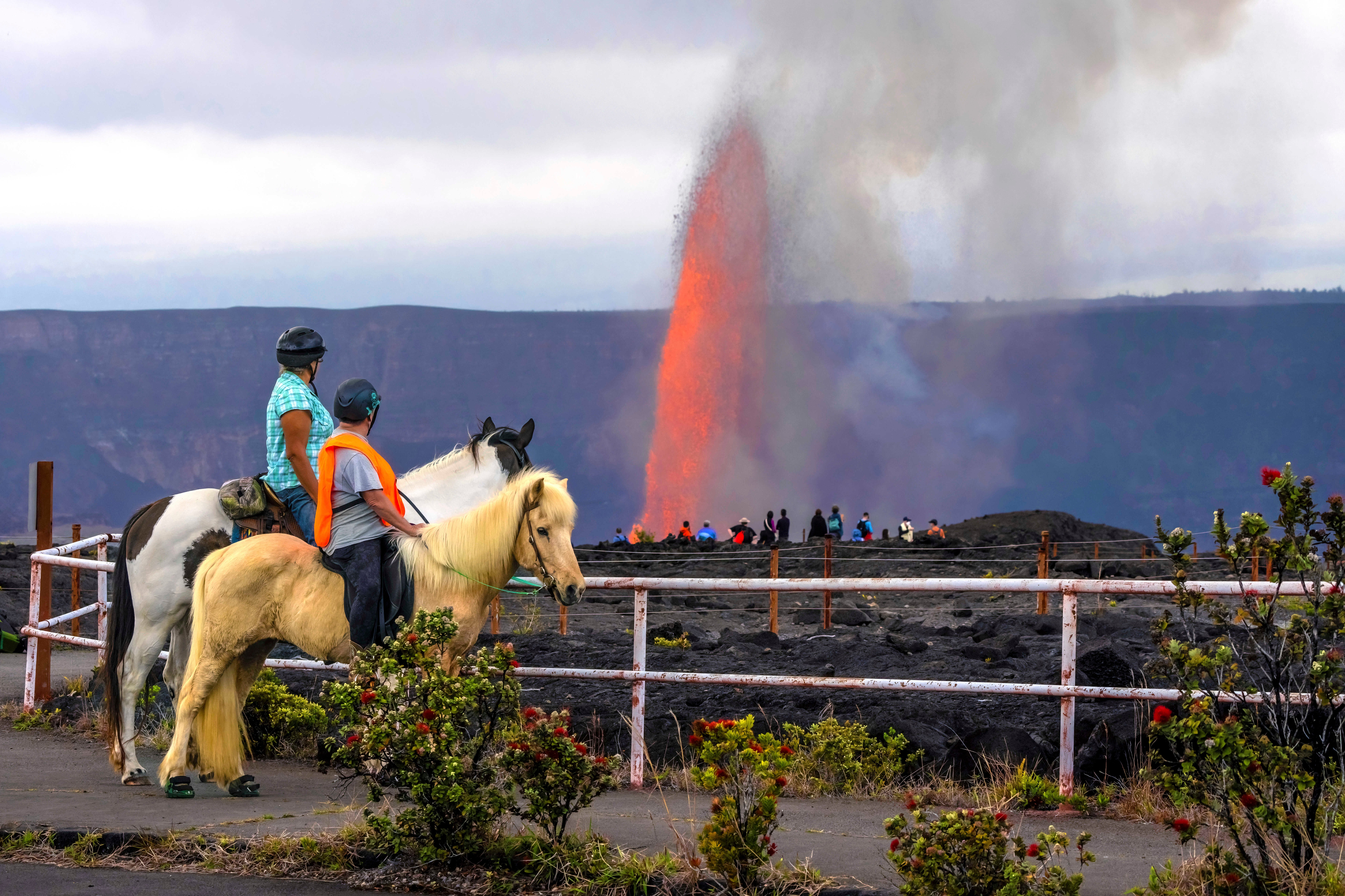 Candi Hololio Johnson, lijevo, i Kim Kozuma, obojica na konju, dok gledaju kako Lava puca iz vrha Caldera u vulkanu Kilauea u Nacionalnom parku Hawaii Volcanoes