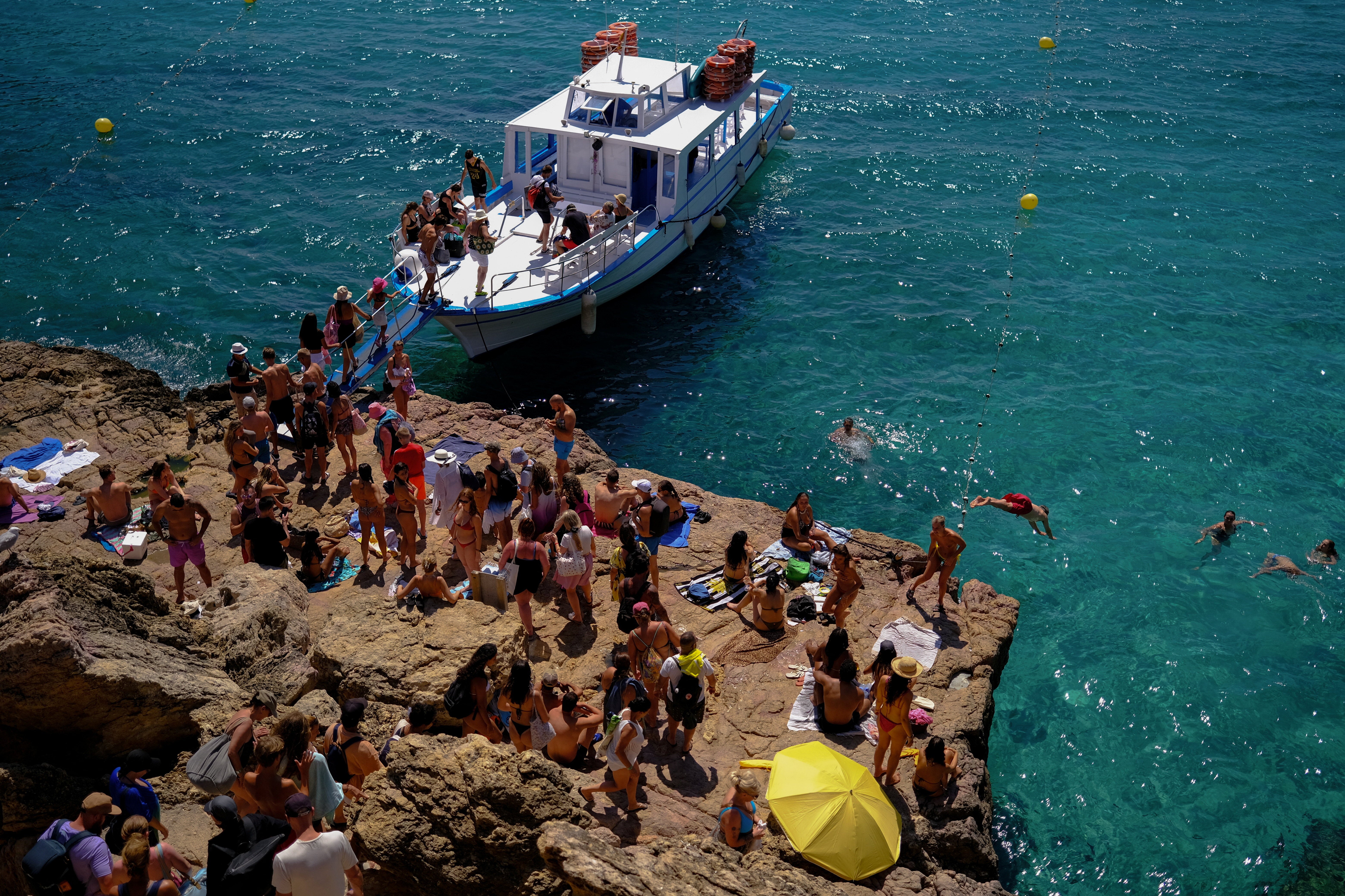 Turisti uživaju u moru jer se drugi ukrcavaju na brod za obilazak plaže na plaži Cala Salata u Sant Antoni de Portmany, Ibiza
