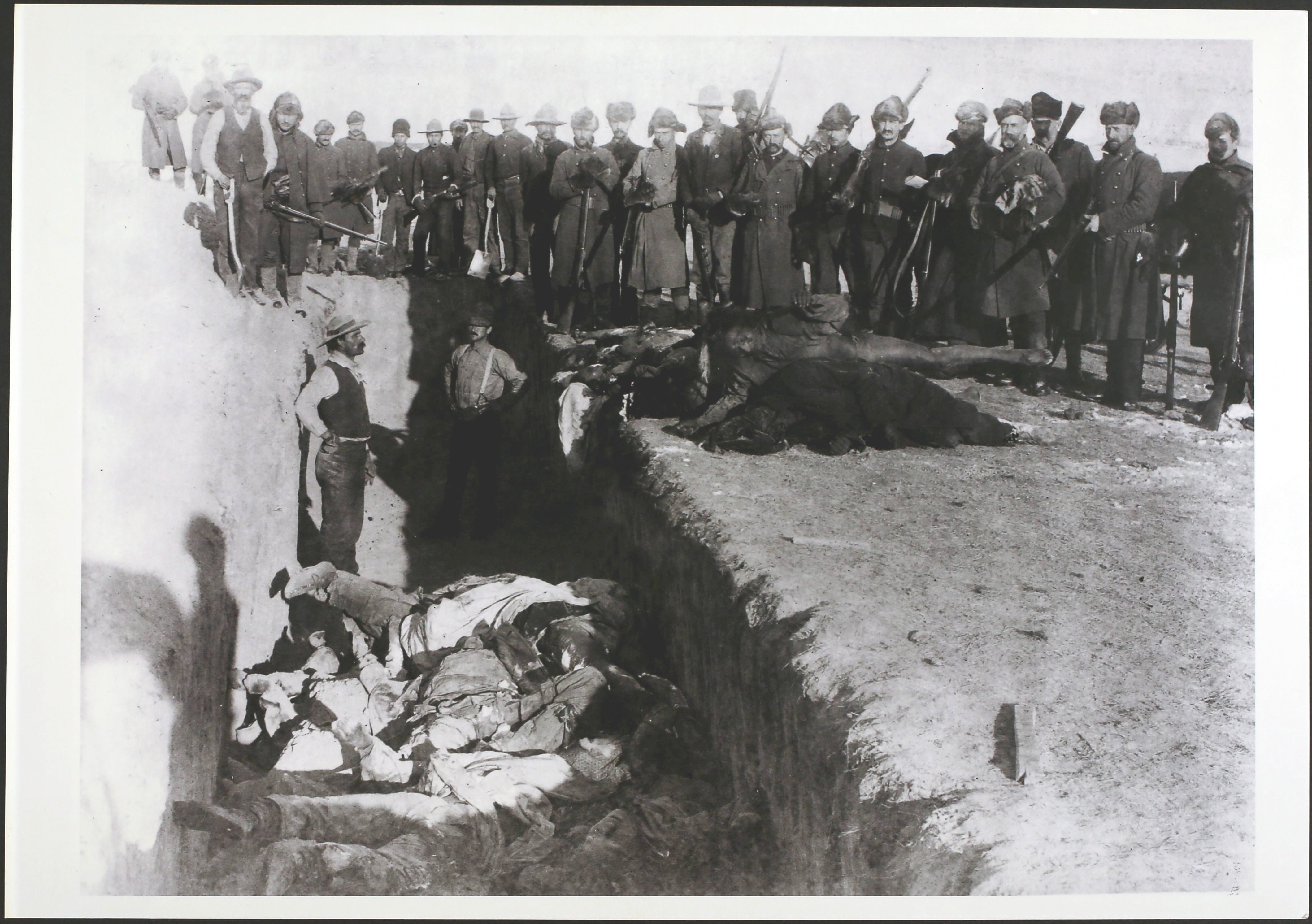 Tijela Lakota Sioux -a bezrezervno su se ugurali u masovni grob koji su se sjekirali u smrznuto tlo Dakota nakon masakra na ranjenom koljenu, Južna Dakota, krajem prosinca 1890. godine. Vojnici i civili gledaju dalje