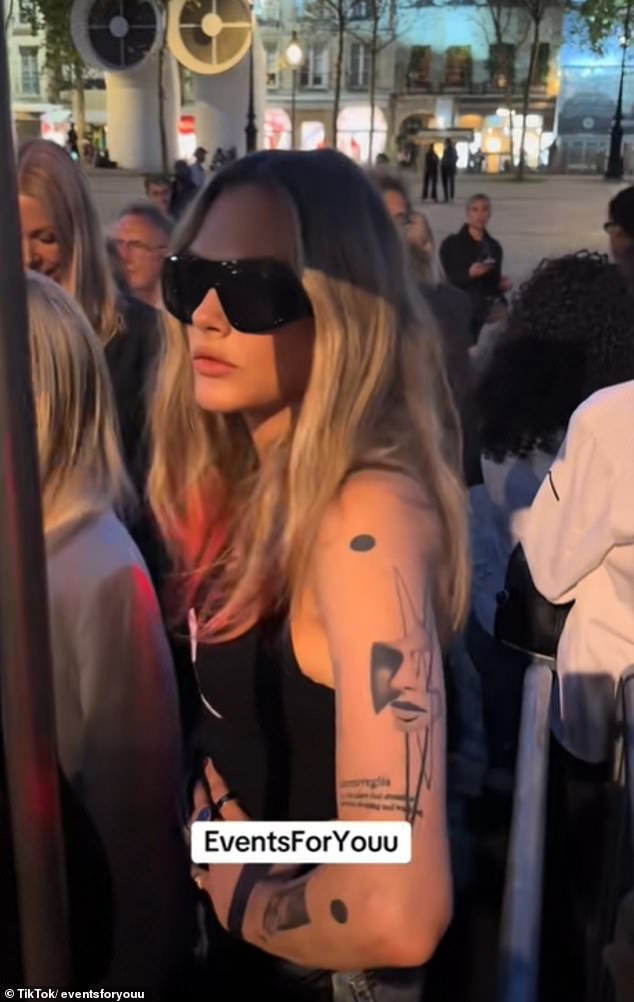 Model, 33, ljuljao je crni tenk i sunčane naočale dok je stajala s rukama na bokovima dok je stajala u redu iza grupe žena