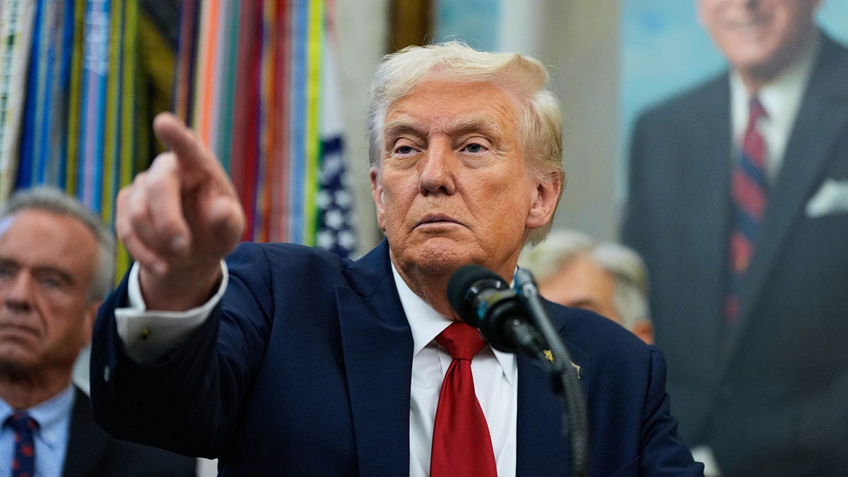 Predsjednik Donald Trump nosi plavo odijelo i crvenu kravatu dok je pokazao novinara u ovalnom uredu