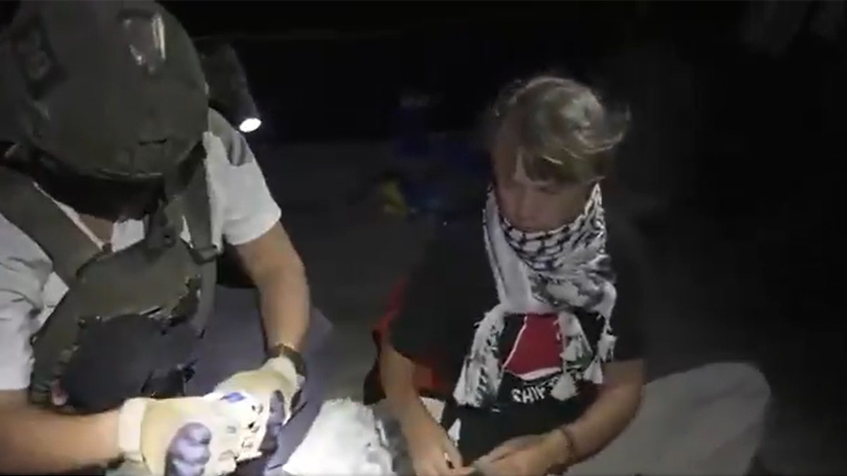 Greta Thunberg, koja nosi crnu košulju i keffiyeh šal, sjedi u blizini izraelskog vojnika u taktičkoj opremi.