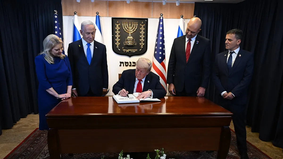 Donald Trump sjedi za stolom u Knessetu dok se upisuje u knjigu gostiju s izraelskim premijerom Benjaminom Netanyahuom i ostalima koji gledaju.