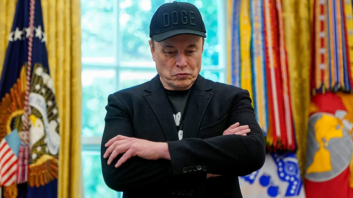 Elon Musk gleda dolje, stoji u Ovalnom uredu prekriženih ruku