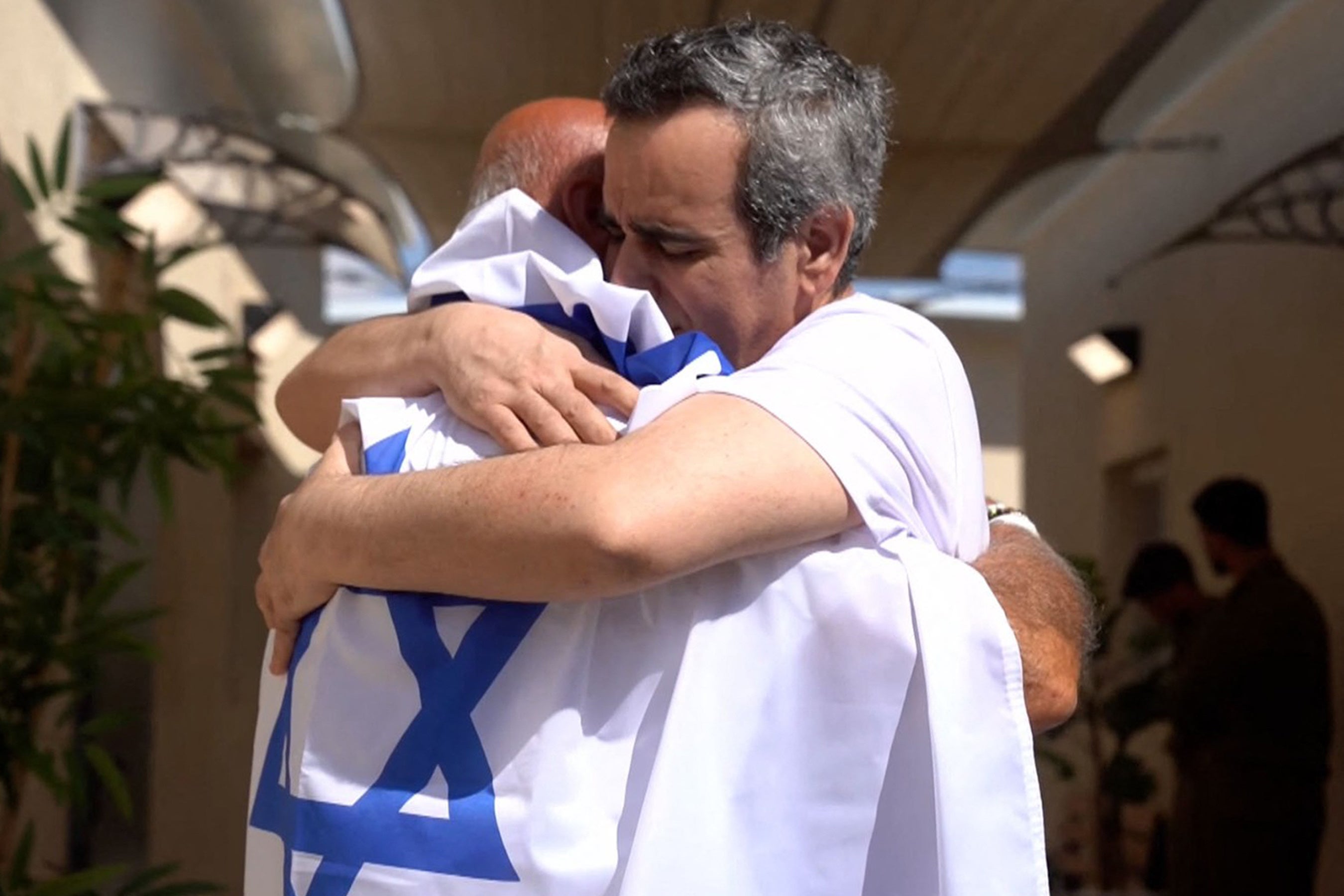 Captive Omri Miran (R) reunited by a member of his family draped in an Israeli flag