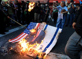 Demonstrator je zapalio znak koji prikazuje američkog predsjednika Donalda Trumpa sa SAD -om i izraelskim zastavama tijekom ožujka u Medellinu u Kolumbiji