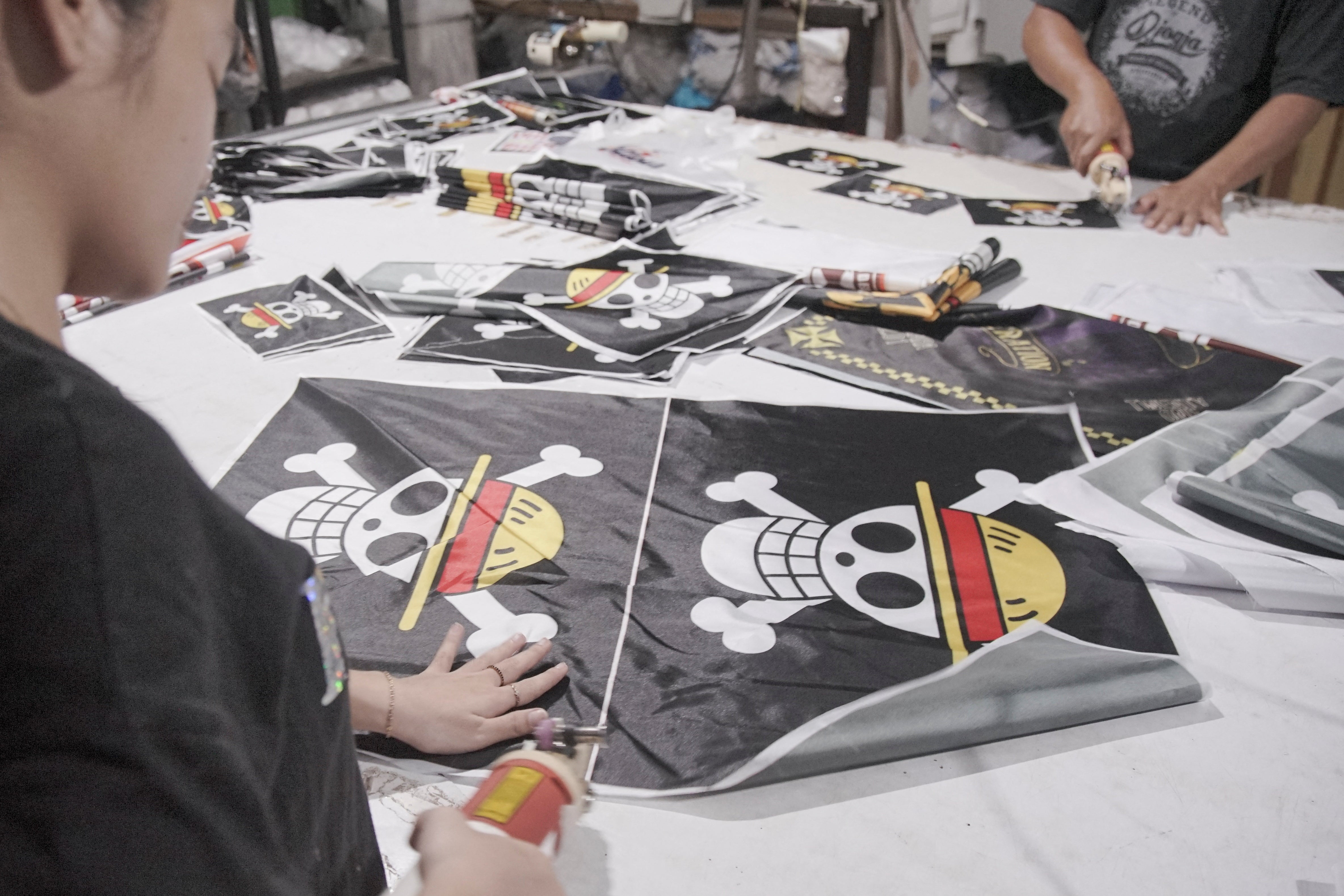 Radnici režu zastave koje prikazuju Jolly Rogera iz popularne japanske anime i manga serije 'One Piece', kod prodavača zastava po narudžbi u Karanganyaru, pokrajina Središnja Java, Indonezija, 7. kolovoza 2025.