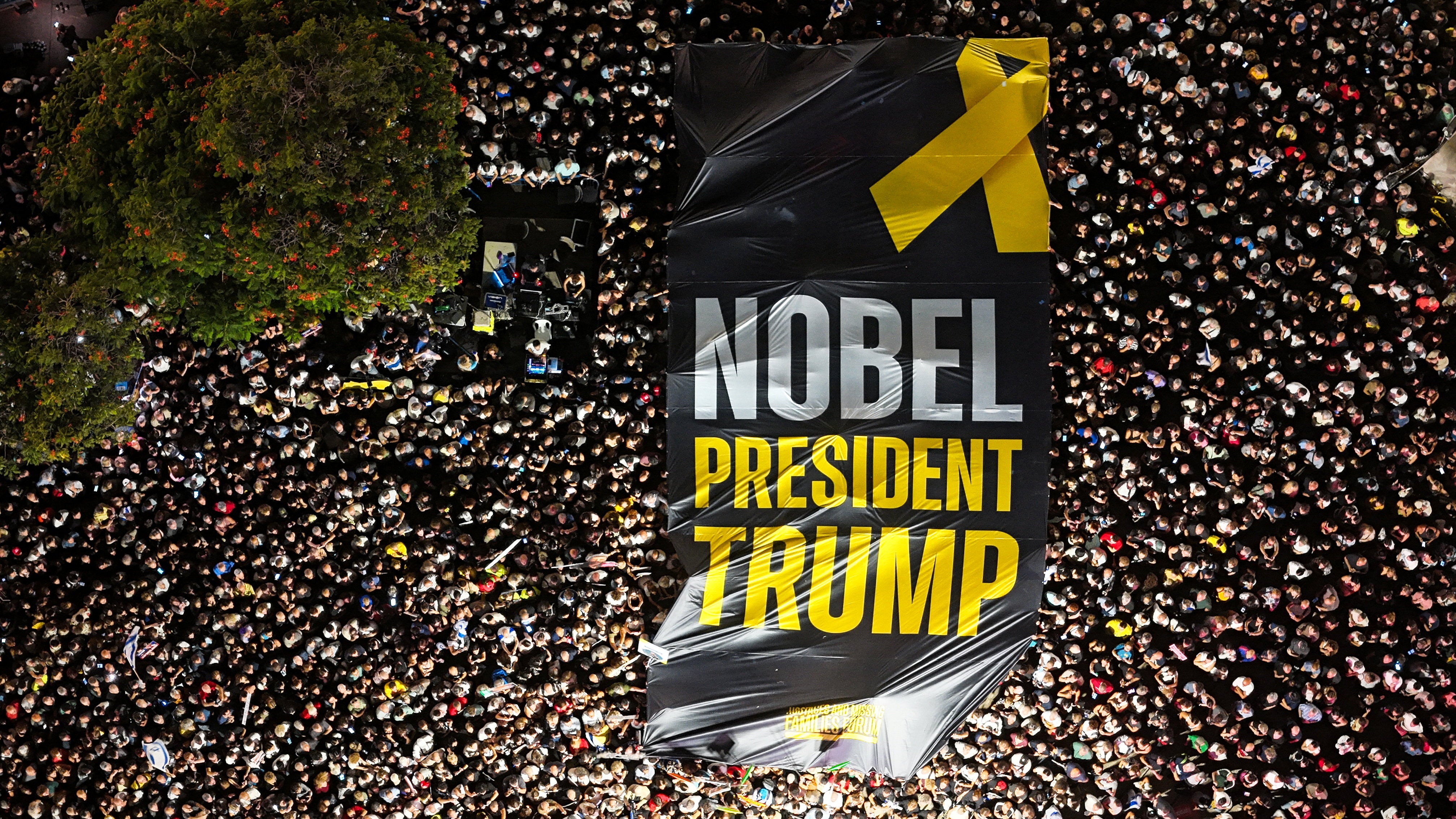 Dronoska fotografija ljudi koji se okupljaju na Trgu talaca dok drže divovski znak koji poziva na napore Donalda Trumpa da bude nagrađen Nobelovom nagradom