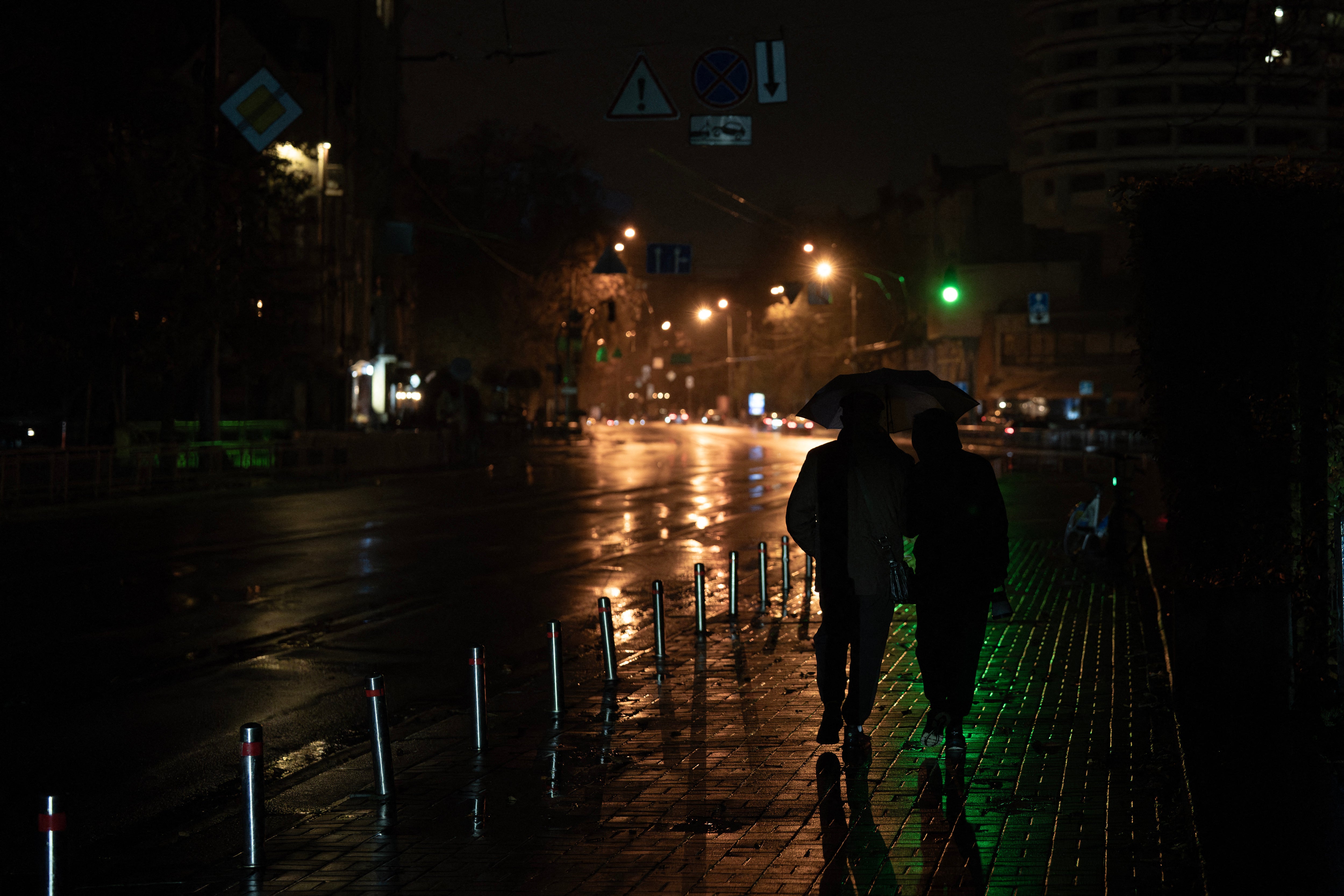 Ljudi hodaju ulicom s kišobranima tijekom prekida struje u Kijevu
