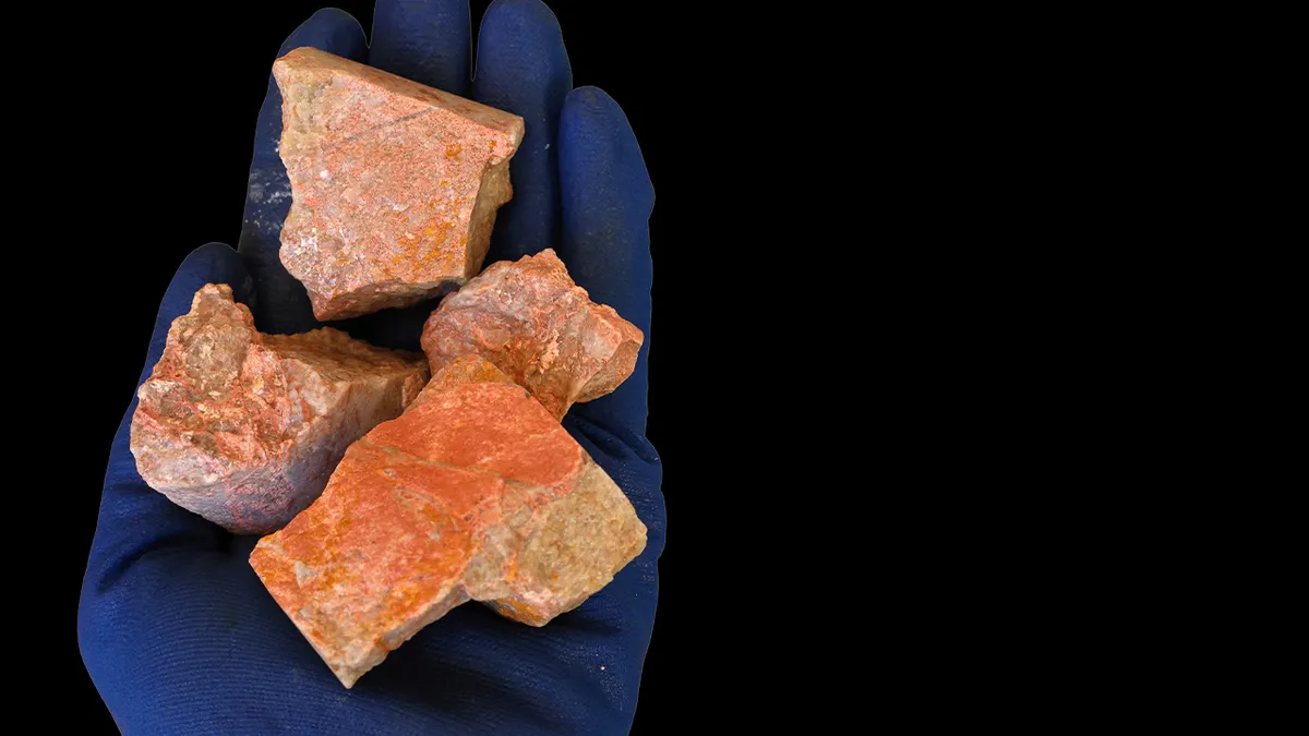 Xenotime ruda rijetkih zemnih elemenata drži se u ruci, plava zaštitna rukavica. Crna pozadina.