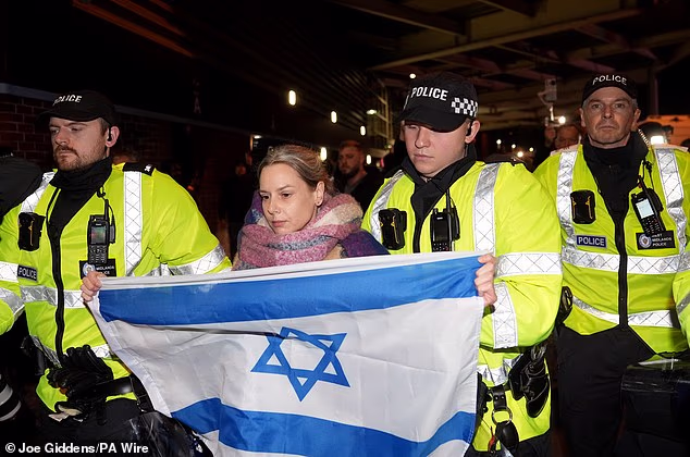 A woman holding an Israeli flag gets dragged away by police officers as tempers flare ahead of Thursday's match